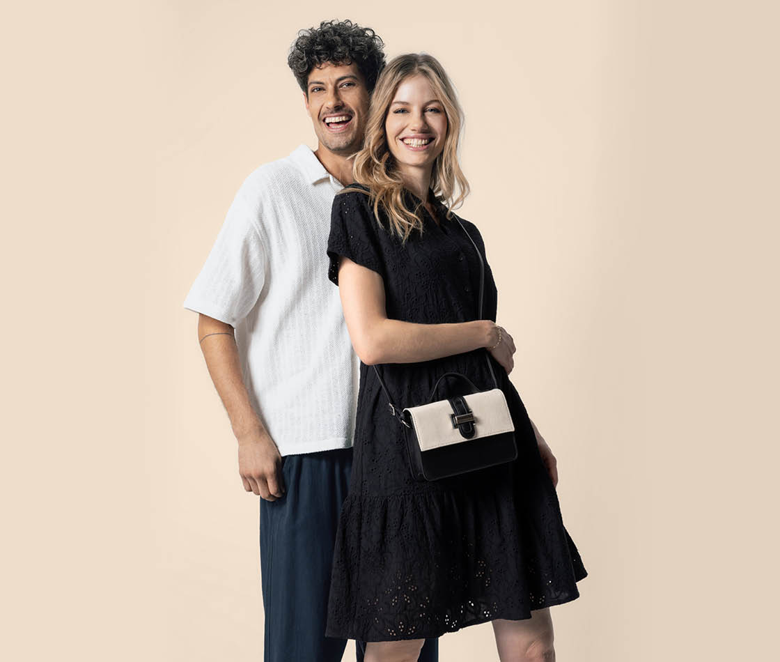 Lächelndes Paar: Frau im schwarzen Kleid mit Umhängetasche, Mann im weißen Hemd dahinter