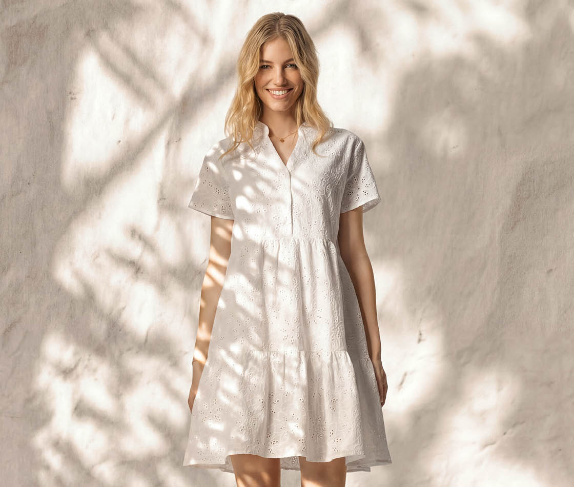 Frau in weißem Stufenkleid vor beiger Wand mit Palmenblattschatten